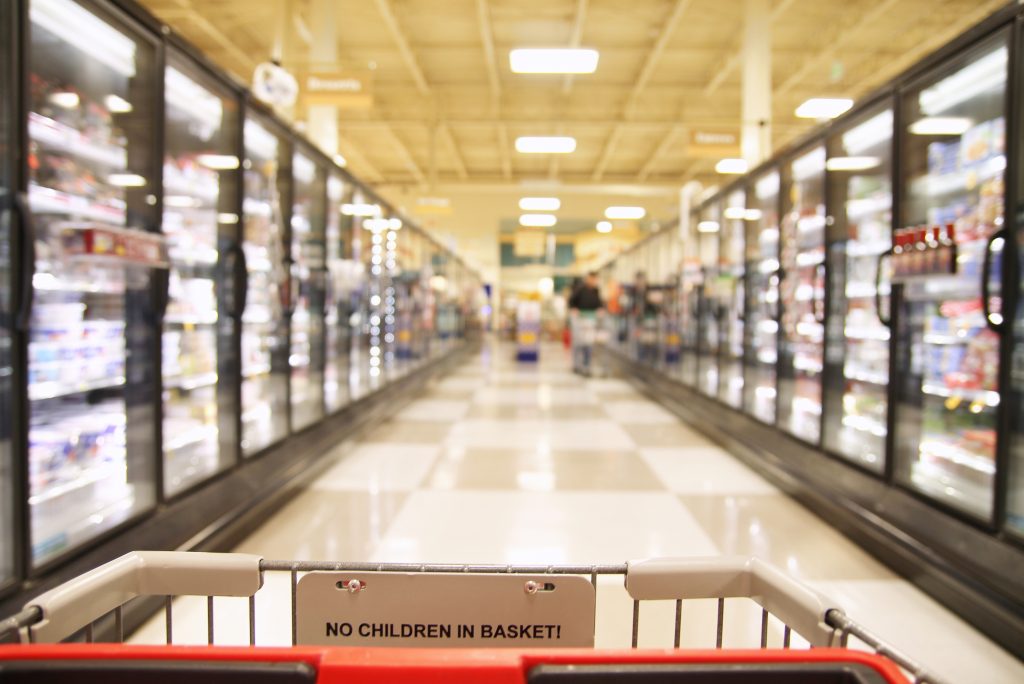 A shopping trolley in a aisle in a grocery store showing frozen foods